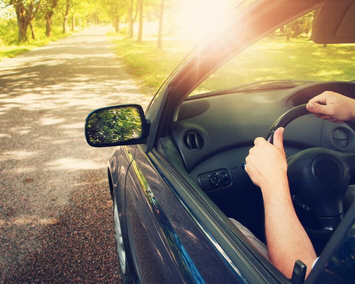 Driver's hands on steering wheel, with driver headed down asphalt road on bright sunny day