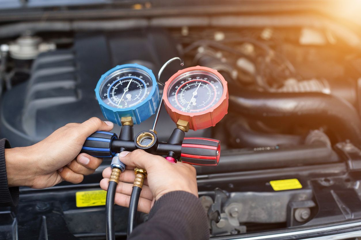 Person holding A/C tester in front of opened car hood.