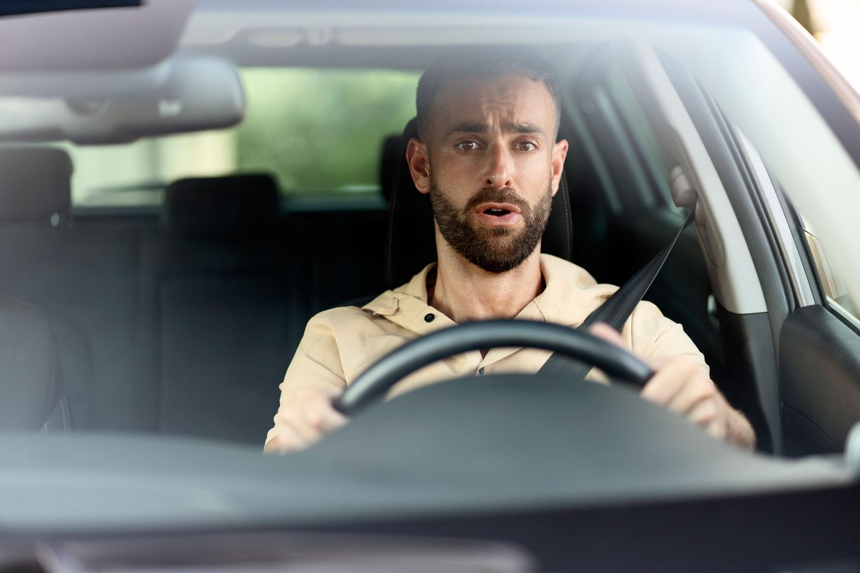 Alarmed man wearing a seatbelt in driver's seat of vehicle.